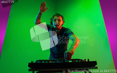 Image of Young caucasian musician in headphones performing on bicolored green-purple background in neon light