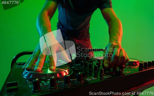 Image of Young caucasian musician in headphones performing on green background in neon light