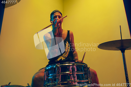 Image of Young caucasian musician inspired performing on yellow background in neon light