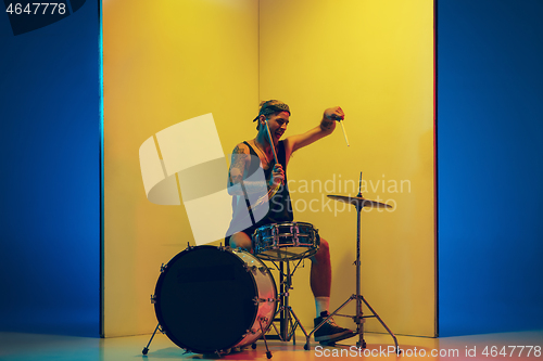 Image of Young caucasian musician inspired performing on yellow background in neon light