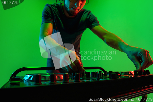Image of Young caucasian musician in headphones performing on green background in neon light