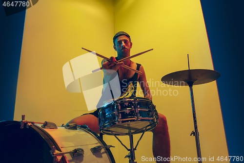 Image of Young caucasian musician inspired performing on yellow background in neon light