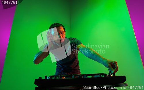 Image of Young caucasian musician in headphones performing on bicolored green-purple background in neon light