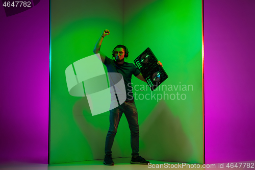 Image of Young caucasian musician in headphones performing on bicolored green-purple background in neon light