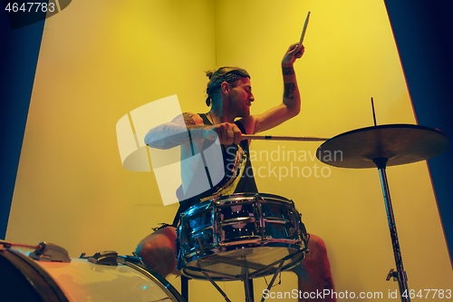 Image of Young caucasian musician inspired performing on yellow background in neon light