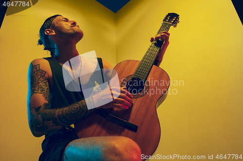 Image of Young caucasian musician inspired performing on yellow background in neon light