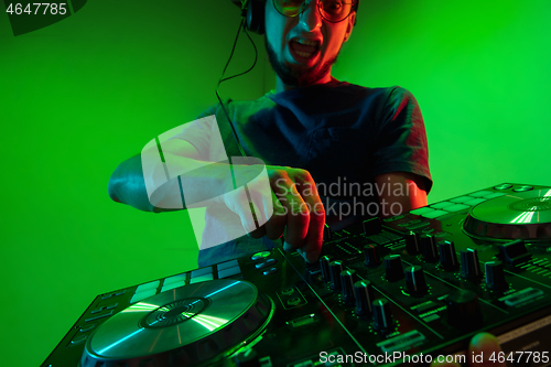 Image of Young caucasian musician in headphones performing on green background in neon light