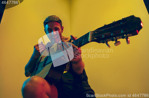 Image of Young caucasian musician inspired performing on yellow background in neon light