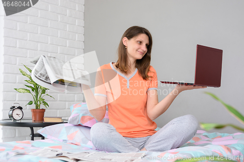 Image of Girl holds newspapers and laptop in her hands, look at laptop