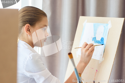 Image of A girl in light clothes sits in front of an easel and draws still life
