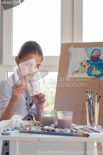Image of Girl examines brush for drawing watercolor paints