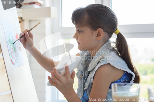 Image of Girl diligently draws a picture on an easel in front of a large window