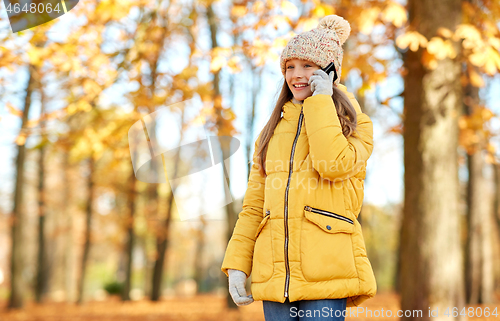 Image of happy girl calling on smartphone at autumn park