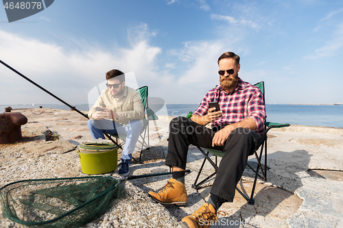 Image of friends with smartphones fishing on pier at sea