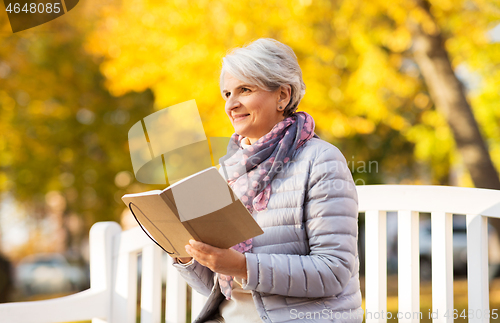 Image of happy senior woman reading diary at autumn park