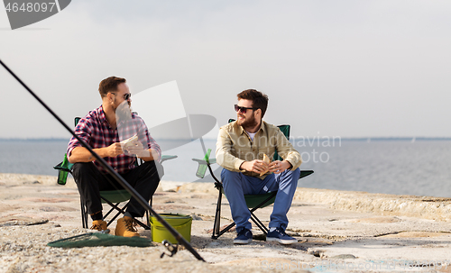 Image of happy friends fishing and eating sandwiches