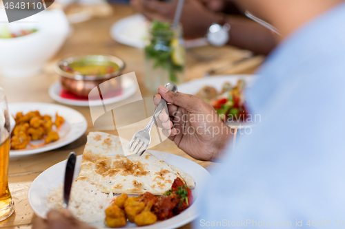 Image of african man eating with friends at restaurant