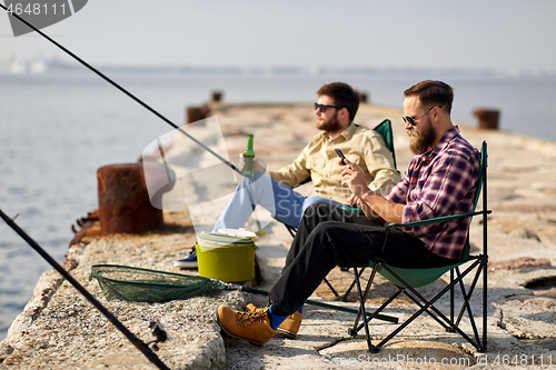 Image of friends with smartphone and beer fishing on pier