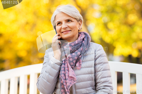 Image of senior woman calling on smartphone at autumn park