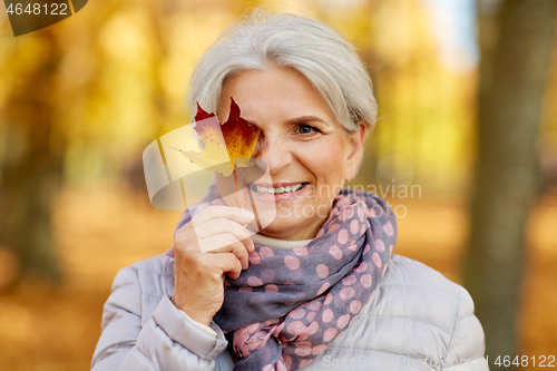 Image of happy senior woman with maple leaf at autumn park