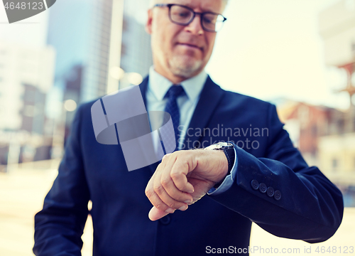 Image of senior businessman with wristwatch on city street