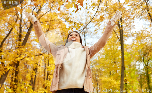 Image of happy woman having fun with leaves in autumn park