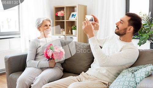 Image of adult son photographing senior mother at home