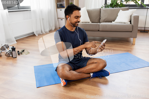 Image of indian man with smartphone on exercise mat at home