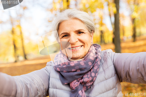 Image of senior woman taking selfie at autumn park