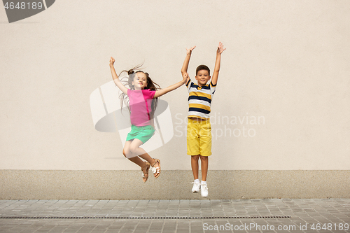 Image of Two smiling kids, boy and girl running together in town, city in summer day