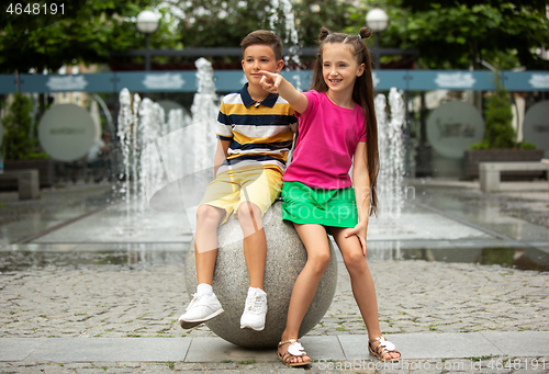 Image of Two smiling kids, boy and girl running together in town, city in summer day