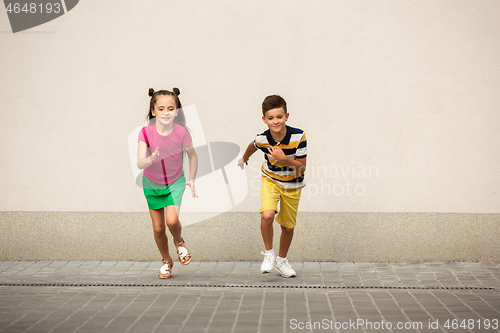 Image of Two smiling kids, boy and girl running together in town, city in summer day