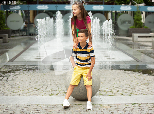 Image of Two smiling kids, boy and girl running together in town, city in summer day