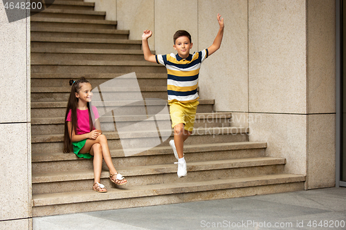 Image of Two smiling kids, boy and girl running together in town, city in summer day