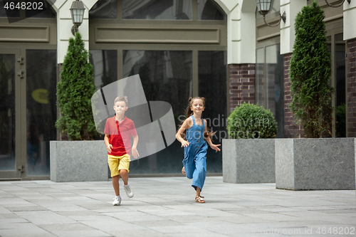 Image of Two smiling kids, boy and girl running together in town, city in summer day