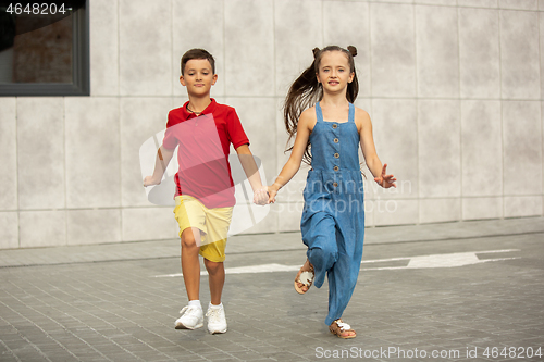 Image of Two smiling kids, boy and girl running together in town, city in summer day