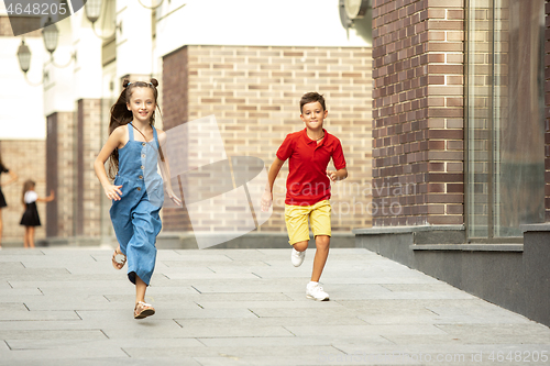 Image of Two smiling kids, boy and girl running together in town, city in summer day