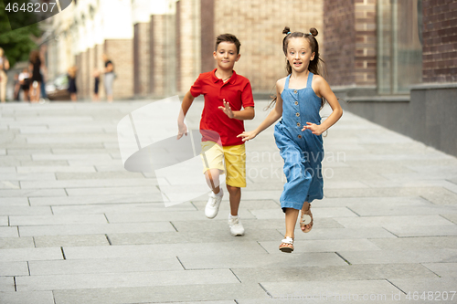 Image of Two smiling kids, boy and girl running together in town, city in summer day