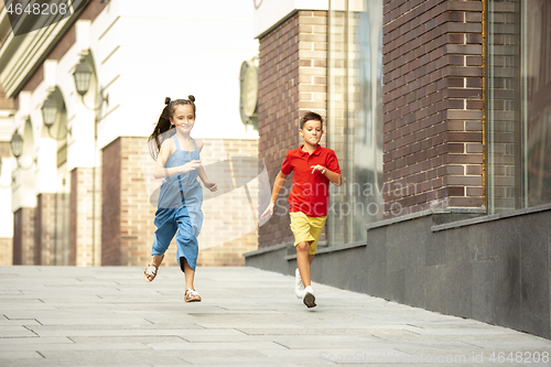 Image of Two smiling kids, boy and girl running together in town, city in summer day