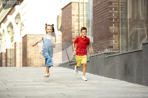 Image of Two smiling kids, boy and girl running together in town, city in summer day