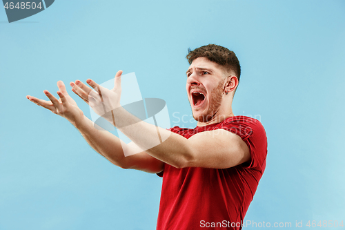 Image of The young emotional angry man screaming on blue studio background