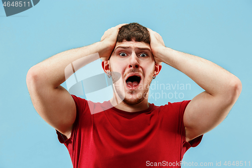 Image of The young emotional angry man screaming on blue studio background