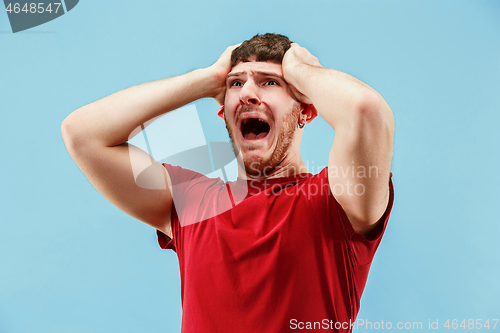 Image of The young emotional angry man screaming on blue studio background