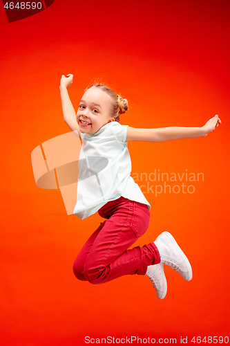 Image of Young happy caucasian teen girl jumping in the air, isolated on red studio background.