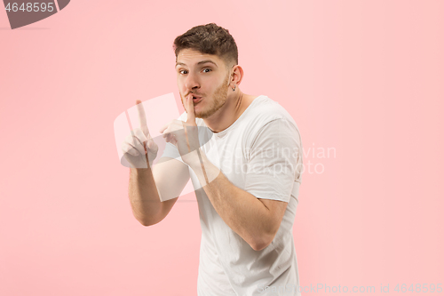 Image of The young man whispering a secret behind her hand over pink background