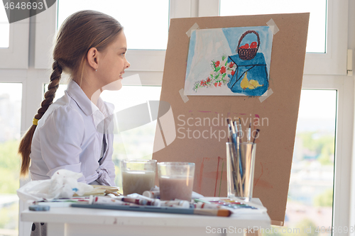 Image of The girl happily looks at her finished drawing hanging on an easel
