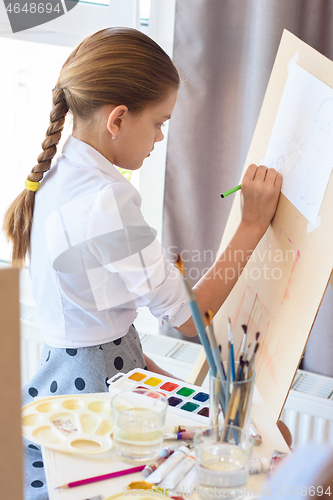Image of Girl is focused on drawing with a pencil on an easel