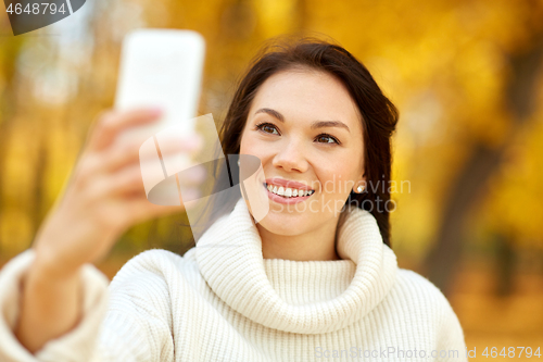 Image of woman taking selfie by smartphone at autumn park