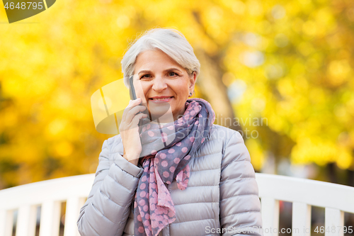 Image of senior woman calling on smartphone at autumn park