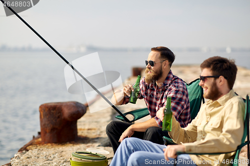 Image of happy friends fishing and drinking beer on pier